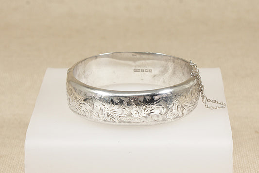 Silver bracelet bangle with intricate designs on a white stand against a beige background