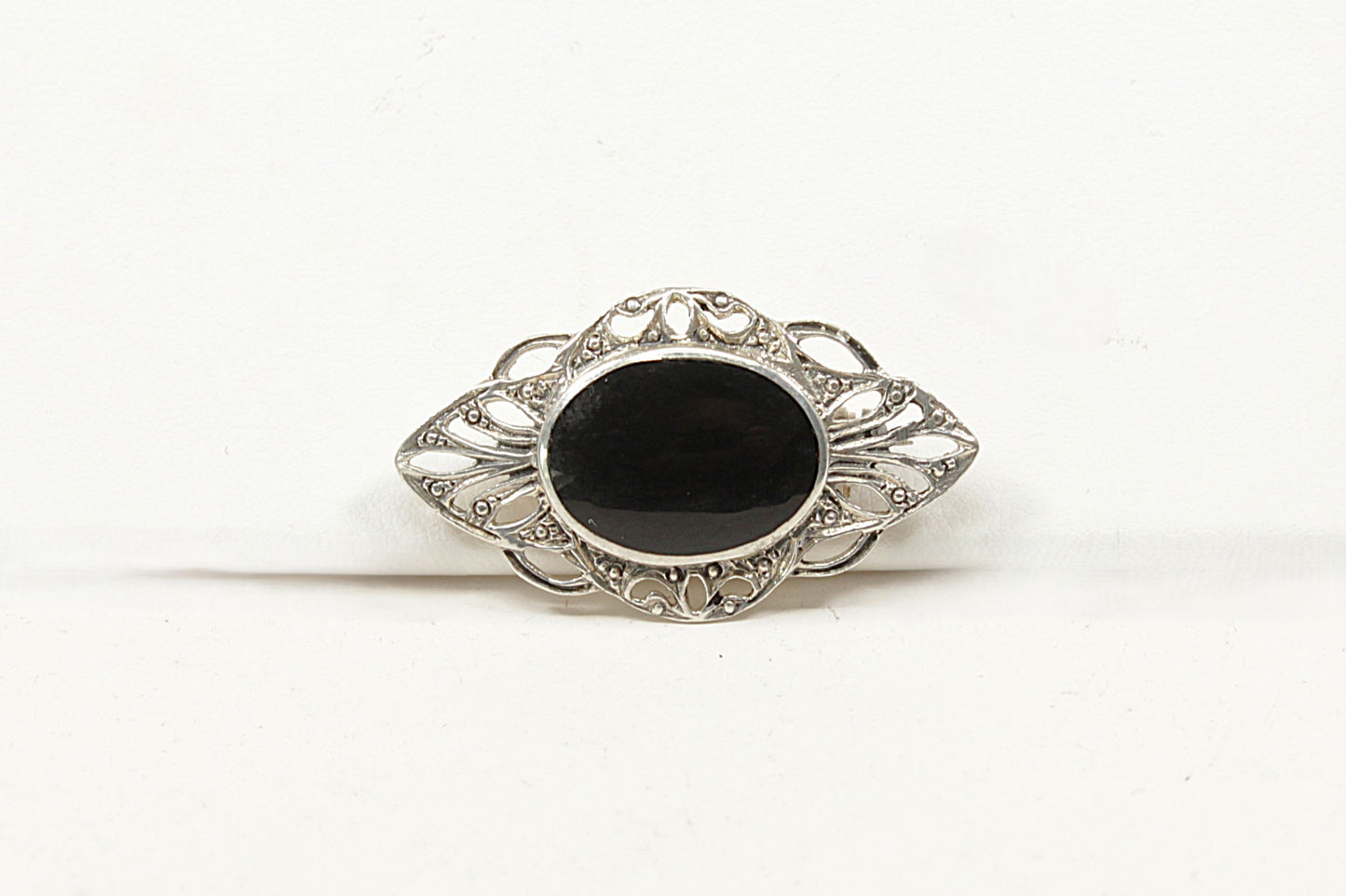 Decorative brooch with a black onyx center and silver intricate design on a white background