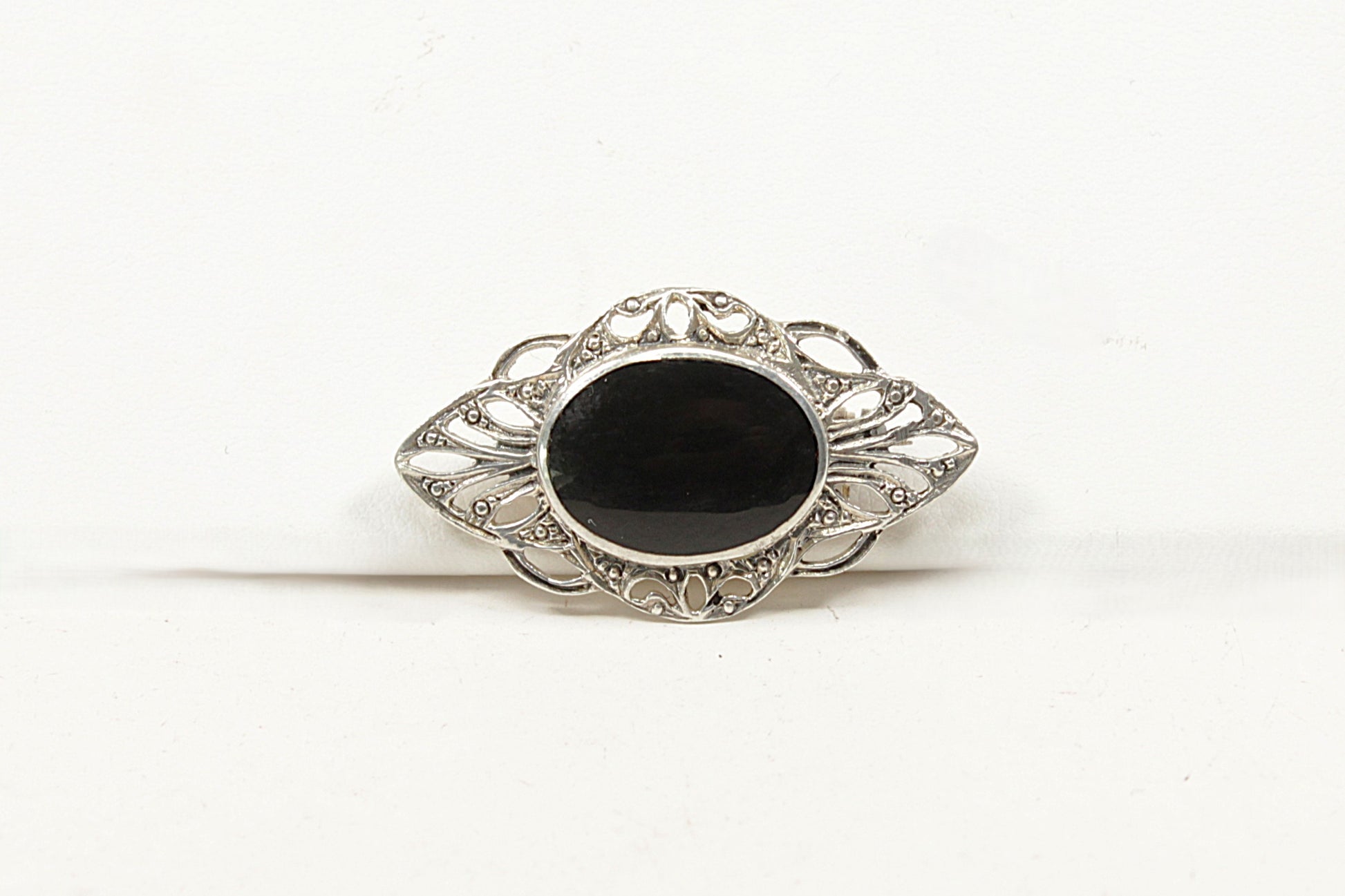 Decorative brooch with a black onyx center and silver intricate design on a white background