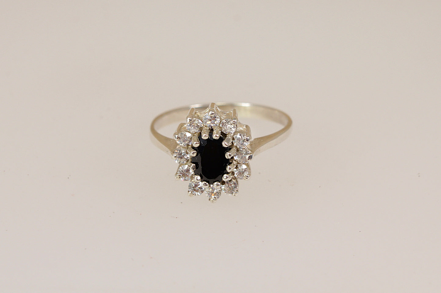 Silver ring with a central blue sapphire gemstone with a halo of cubic ziconia gemstones on a beige background