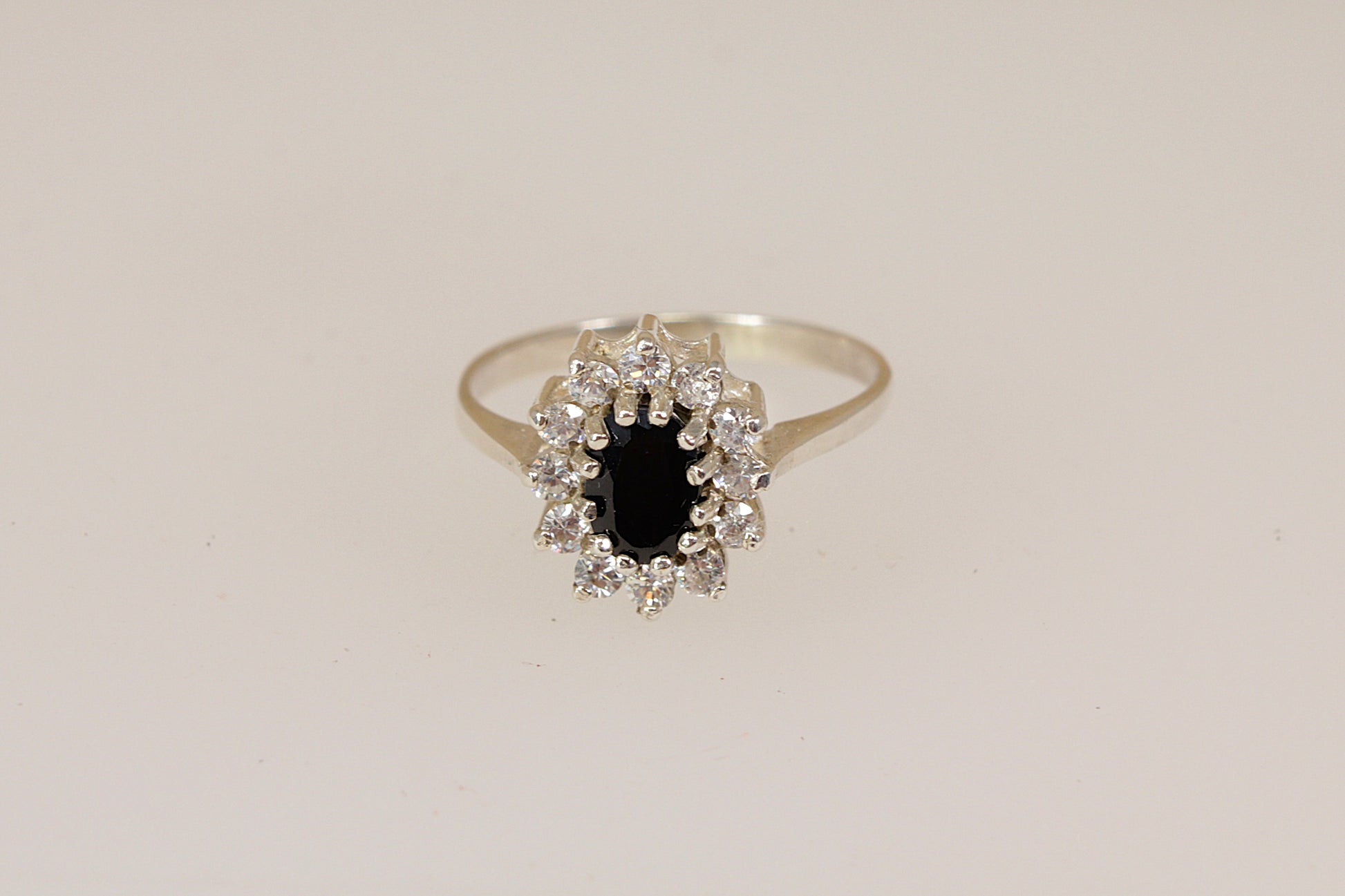 Silver ring with a central blue sapphire gemstone with a halo of cubic ziconia gemstones on a beige background