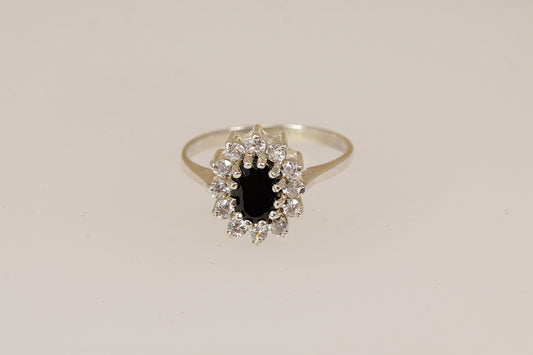 Silver ring with a central blue sapphire gemstone with a halo of cubic ziconia gemstones on a beige background
