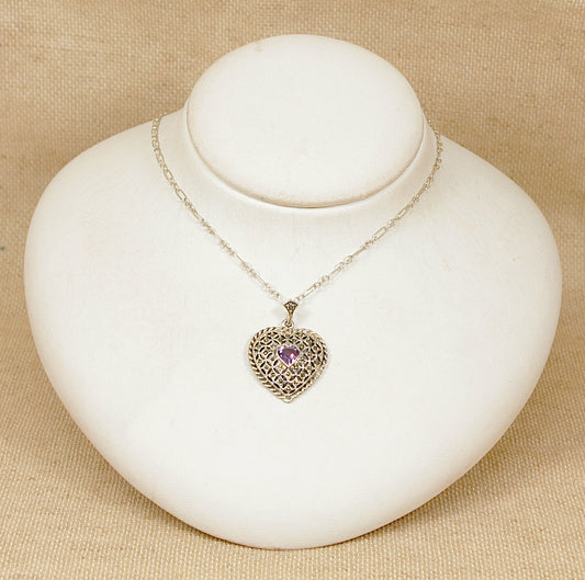 Necklace with a heart-shaped pendant  with a central faceted purple amethyst  on a white stand against a beige background