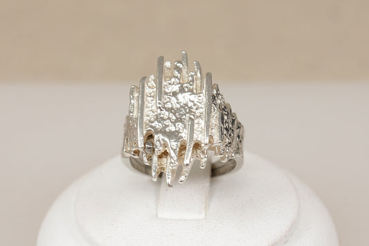 A textured  brutalist sterling silver ring displayed on a white ring stand against a soft beige background.