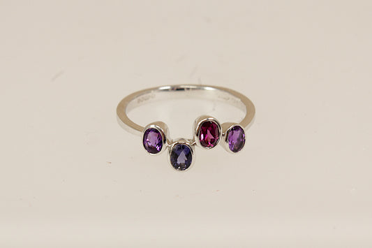 9ct White Gold Multi Gemstone Ring, A delicate and modern 9ct White Gold ring, featuring four oval bezel-set gemstones arranged in a stylish, irregular line across the band. The design includes two vibrant Amethysts, a deep Blue Iolite, and a rich Garnet, full London hallmarks for 2005, UK Finger size: O.